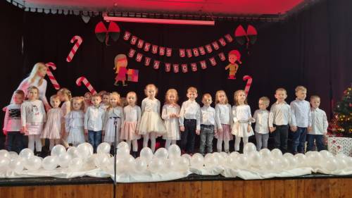 Dzieci na scenie w galowych strojach śpiewające piosenki